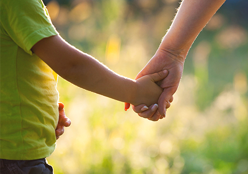 adult holding hand of young child in the sunshine