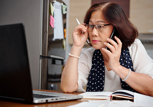 Senior reviewing information on laptop while on mobile phone