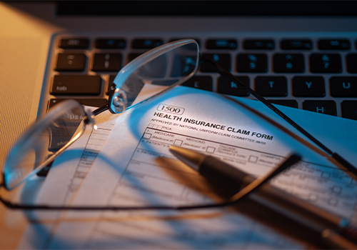 Health insurance claim form on keyboard with pen and eyeglasses on top