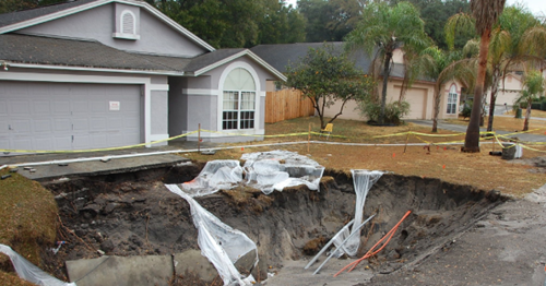 Sinkhole Deductible Front yard sinkhole Large sinkhole in the driveway of a home in a suburban neighborhood