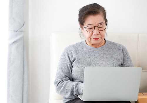 Asian female senior using laptop on sofa