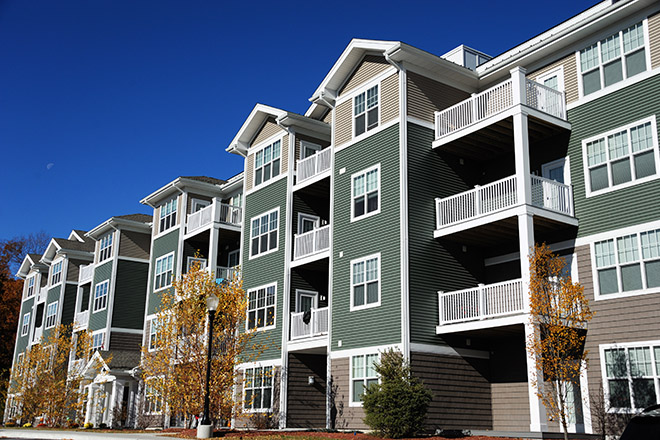 outside view of beige and gray three-story apartment building with trees in front