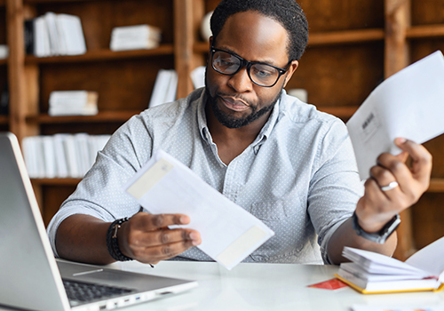 budget-sheet_thumb Black man sitting in front of laptop, worried looking at bills